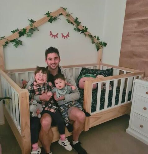 Picture of family sitting on a bed base off the floor, with white rails and back house frame